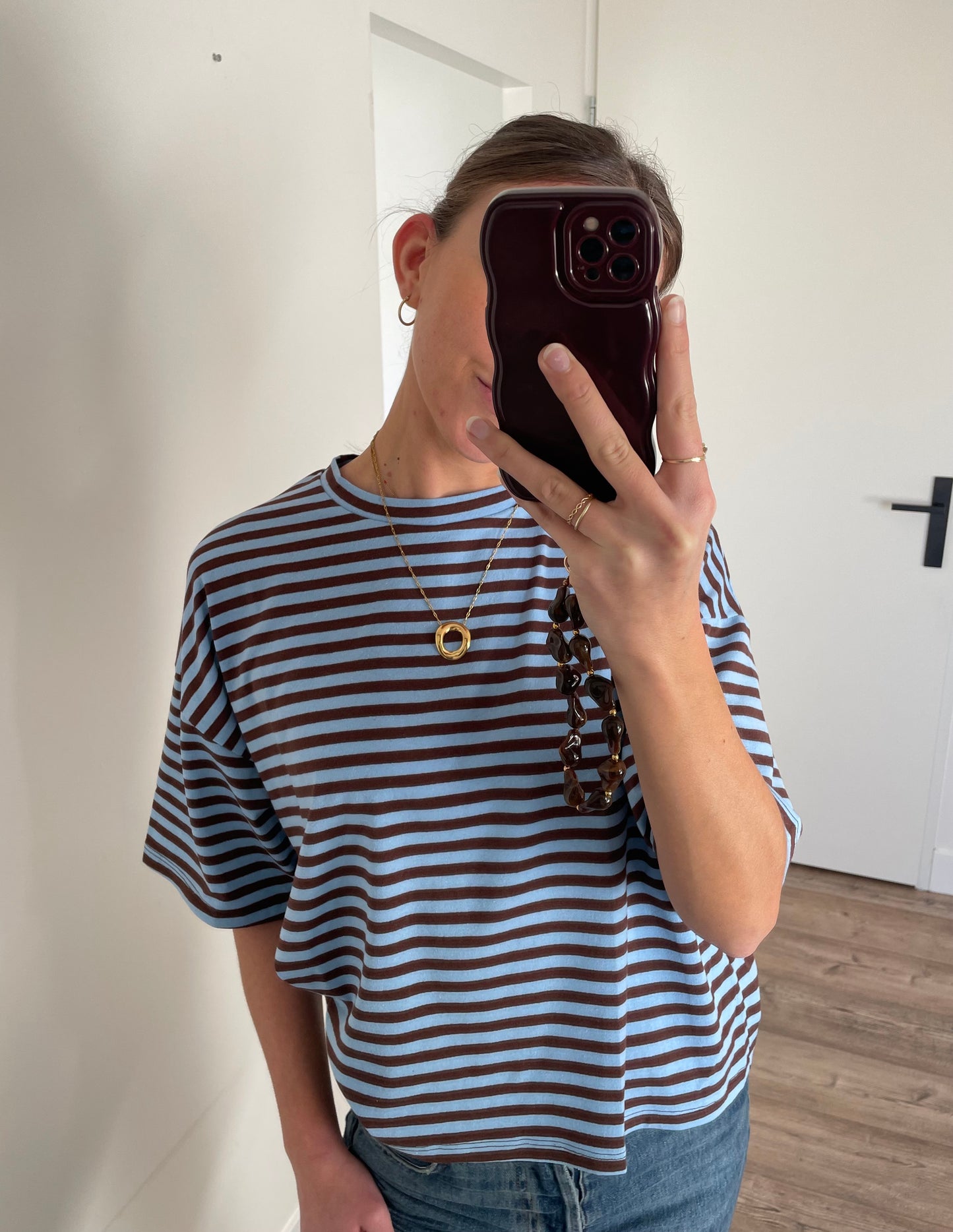 Gestreept oversized shirt voor dames geombineerd met gouden lange ketting en bruin telefoonkoord