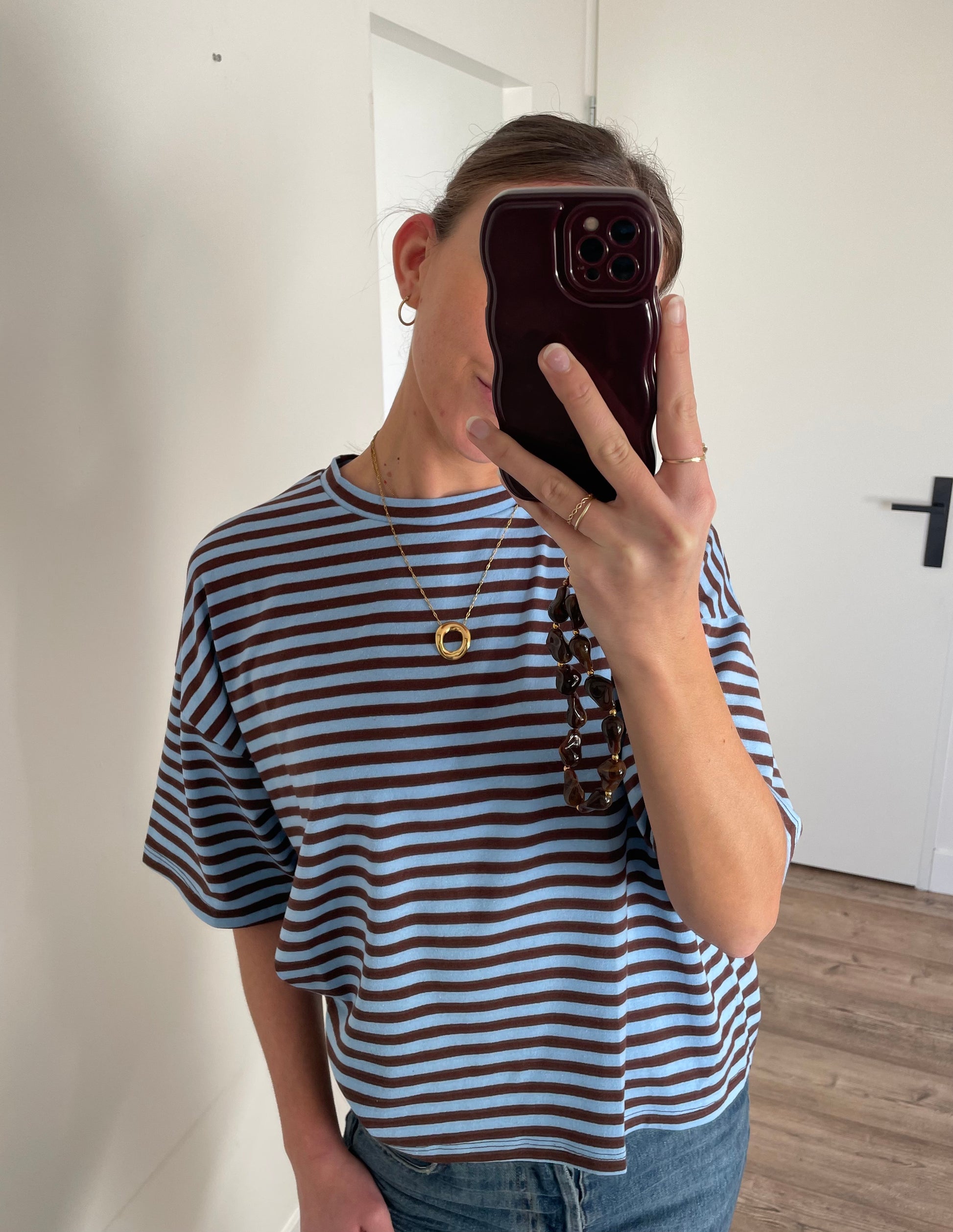 Gestreept oversized shirt voor dames geombineerd met gouden lange ketting en bruin telefoonkoord