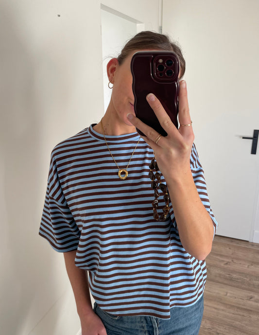 Gestreept oversized shirt voor dames geombineerd met gouden lange ketting en bruin telefoonkoord